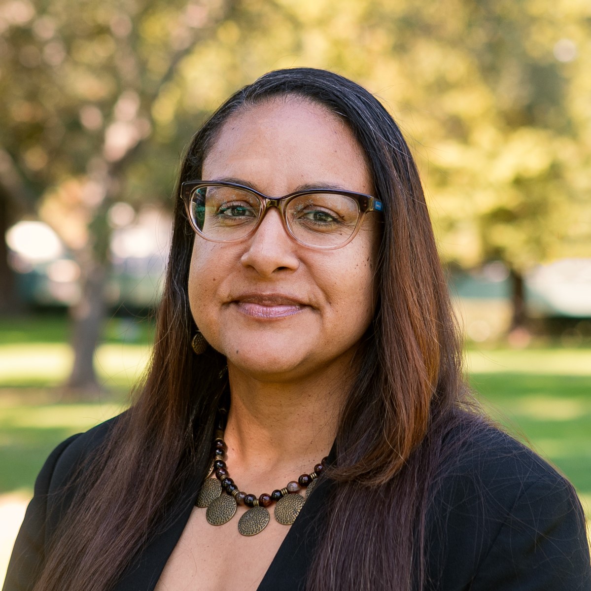 Kim Johnson with medium length straight dark hair, wearing eyeglasses, a necklace, and a dark blazer